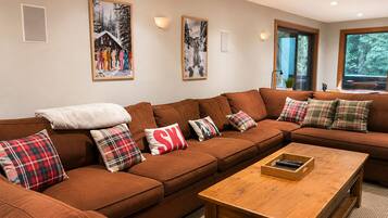 Ein gemütliches Wohnzimmer mit einem braunen Ecksofa, karierten Kissen und einem Holztisch.