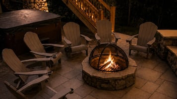Une terrasse extérieure avec des fauteuils Adirondack, un foyer en pierre et un escalier en bois.