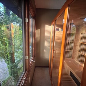 Ein schmaler Flur mit Holzvertäfelung, einem Fenster mit Vorhängen und einem Sauna-Bereich inklusive Bedienfeld.