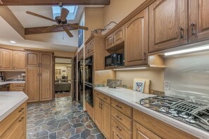 Eine Küche mit Holzausstattung, Steinboden, Gasherd und Deckenventilator.