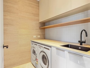 A compact kitchen with a washing machine, a sink, and wooden shelves. - Rosedale House Beachside Luxury Coastal Retreat (Rosedale)
