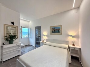 A bedroom with a bed, bedside tables, a dresser, a potted plant, a framed picture, and a window with a view. - Belvedere Fontepatri: the view of your dreams near Florence (Lastra a Signa)