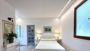 Une chambre à coucher moderne, avec un lit, des tables de chevet, une plante en pot et une porte donnant sur une autre pièce.
