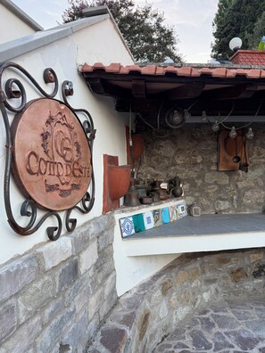 Un'area cucina esterna rustica con un muro in pietra, un piano di lavoro piastrellato e diversi utensili da cucina.