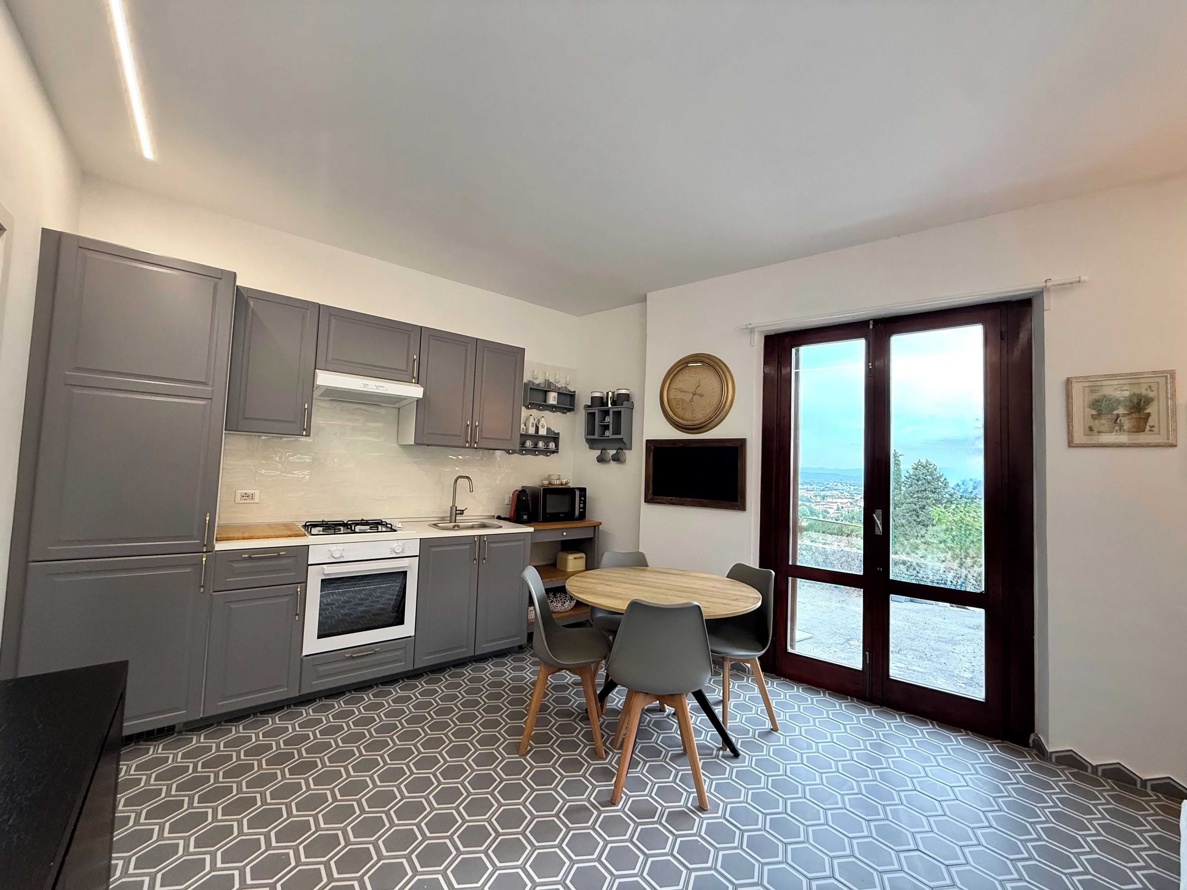 Una cucina compatta con mobili grigi, un fornello e un'area pranzo con un tavolo rotondo e sedie.
