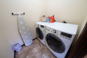 A laundry area with two washing machines, a drying rack, and laundry supplies.