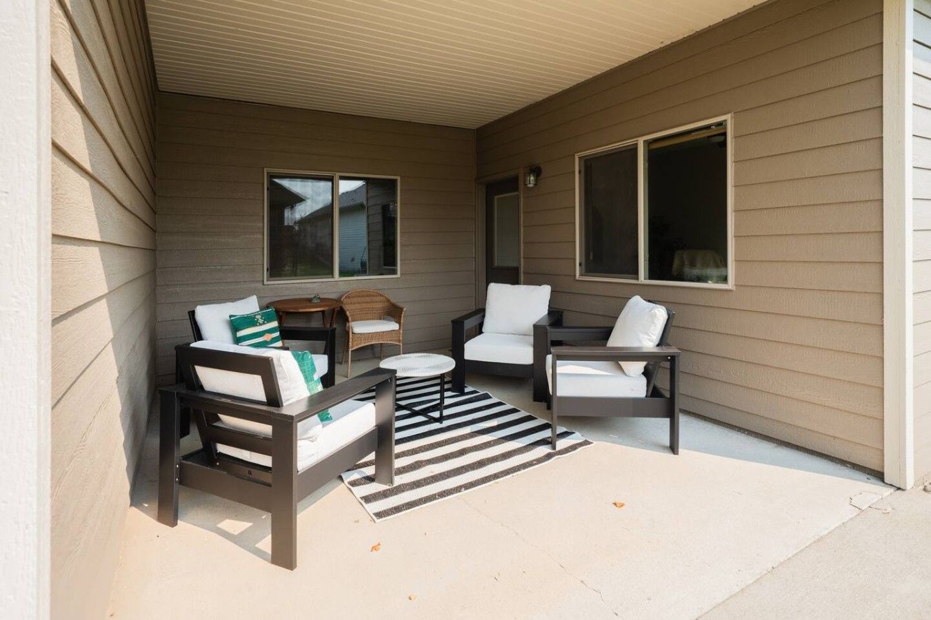 A covered outdoor seating area with two sofas, a small round table, and a wicker chair.