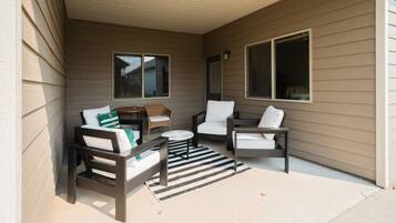 A covered outdoor seating area with two sofas, a small round table, and a wicker chair.