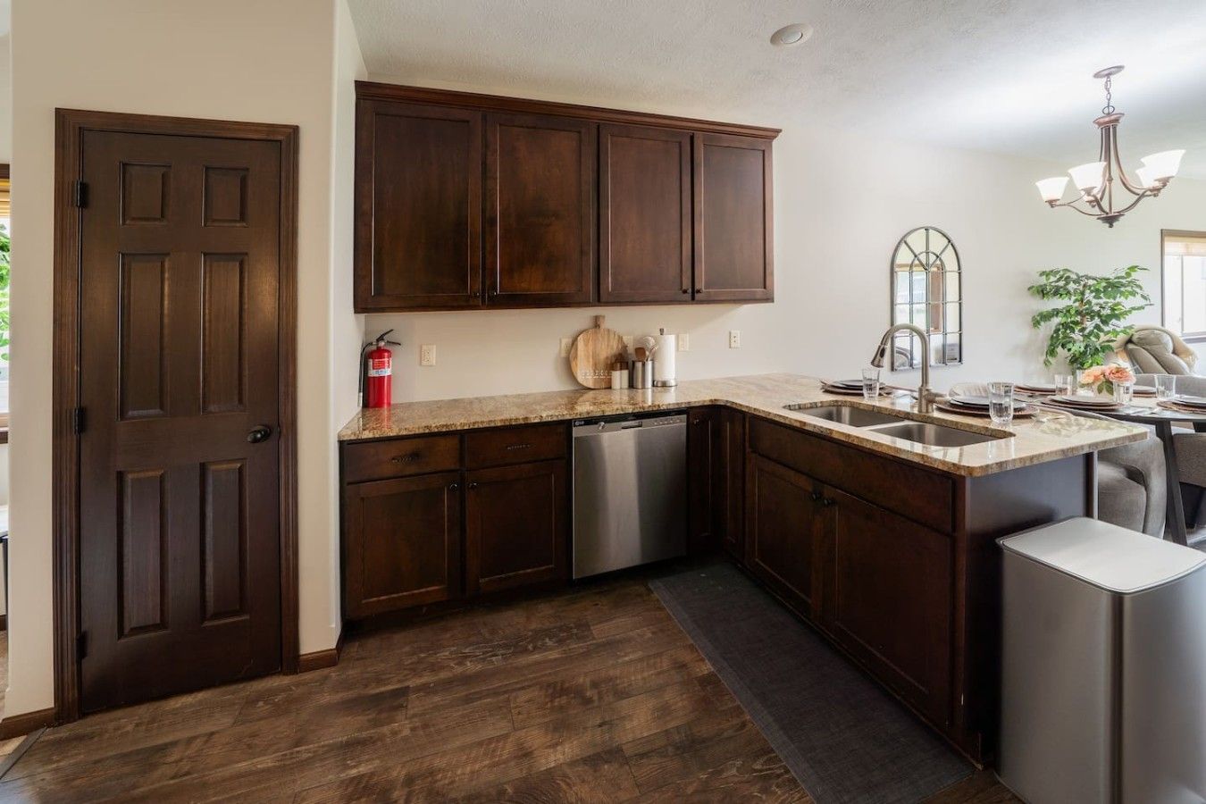 Una cocina con armarios de madera oscura, lavavajillas de acero inoxidable, encimera de granito y pileta integrada.