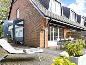 Une maison moderne avec une façade en briques, une porte d’entrée en verre et un patio comprenant un coin salon avec un fauteuil et une table.