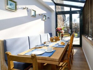 A dining area with a long wooden table set for breakfast, a bench, and a view through a large window. - Holiday Home With 2 Bedrooms (Sylt)