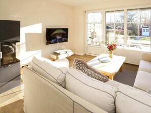 A modern living room with a sofa, a coffee table, a TV, and a window with a view of the outside. - Holiday Home With 2 Bedrooms (Sylt)