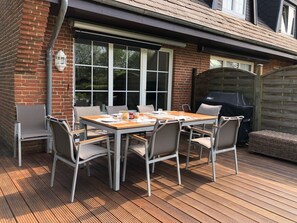 An outdoor patio with a wooden table and chairs, a barbecue grill, and a brick wall. - Holiday Home With 2 Bedrooms (Sylt)