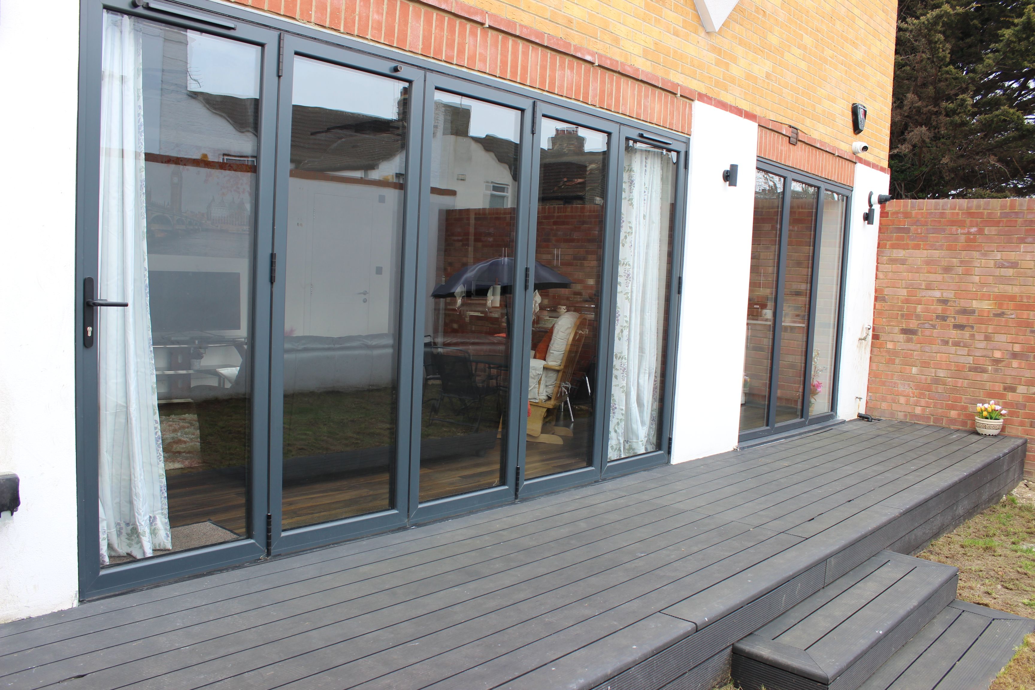 Et moderne hus med store skydedøre, en træterrasse og en murstensvæg.