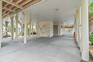 A spacious covered area with a concrete floor and white structural beams. - 5BR | Sleeps 14 | Pool | Steps To The Beach | 601B (Murrells Inlet)