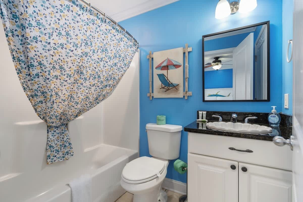 A bathroom with a blue wall, a white toilet, a white sink with a black countertop, and a shower curtain with a floral pattern.