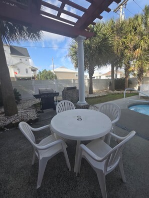 Une terrasse extérieure avec une table ronde et quatre chaises, un barbecue et une piscine.