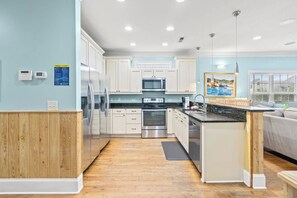 A modern kitchen with white cabinets, stainless steel appliances, and a wooden accent wall. - 5BR | Sleeps 14 | Pool | Steps To The Beach | 601B (Murrells Inlet)
