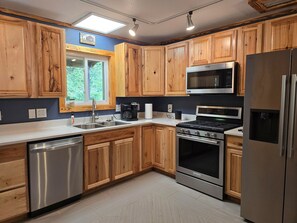 A kitchen with wooden cabinets, stainless steel appliances, a dishwasher, and a window with a view of greenery.