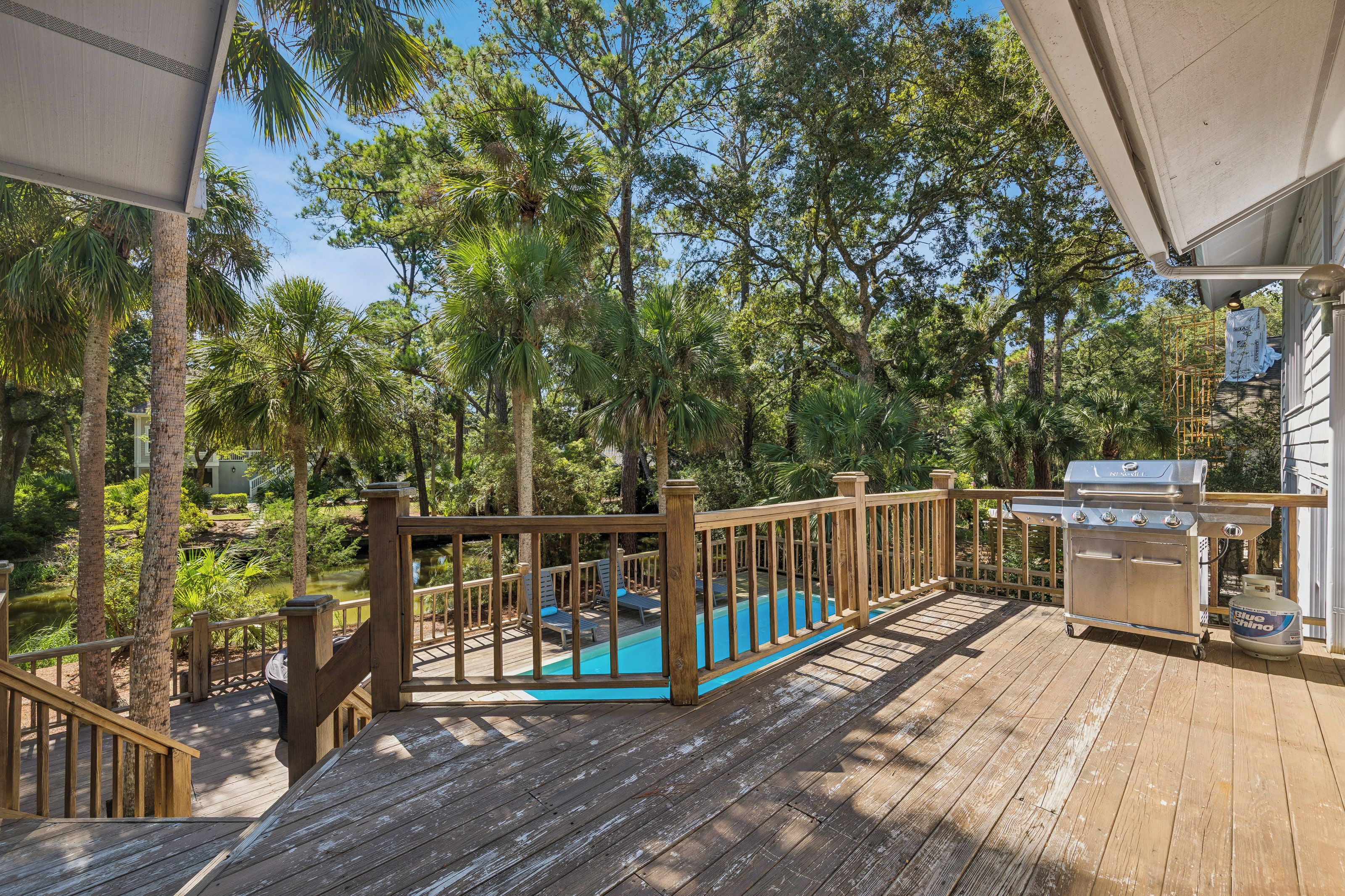 A wooden deck with a pool, surrounded by trees and a barbecue grill.