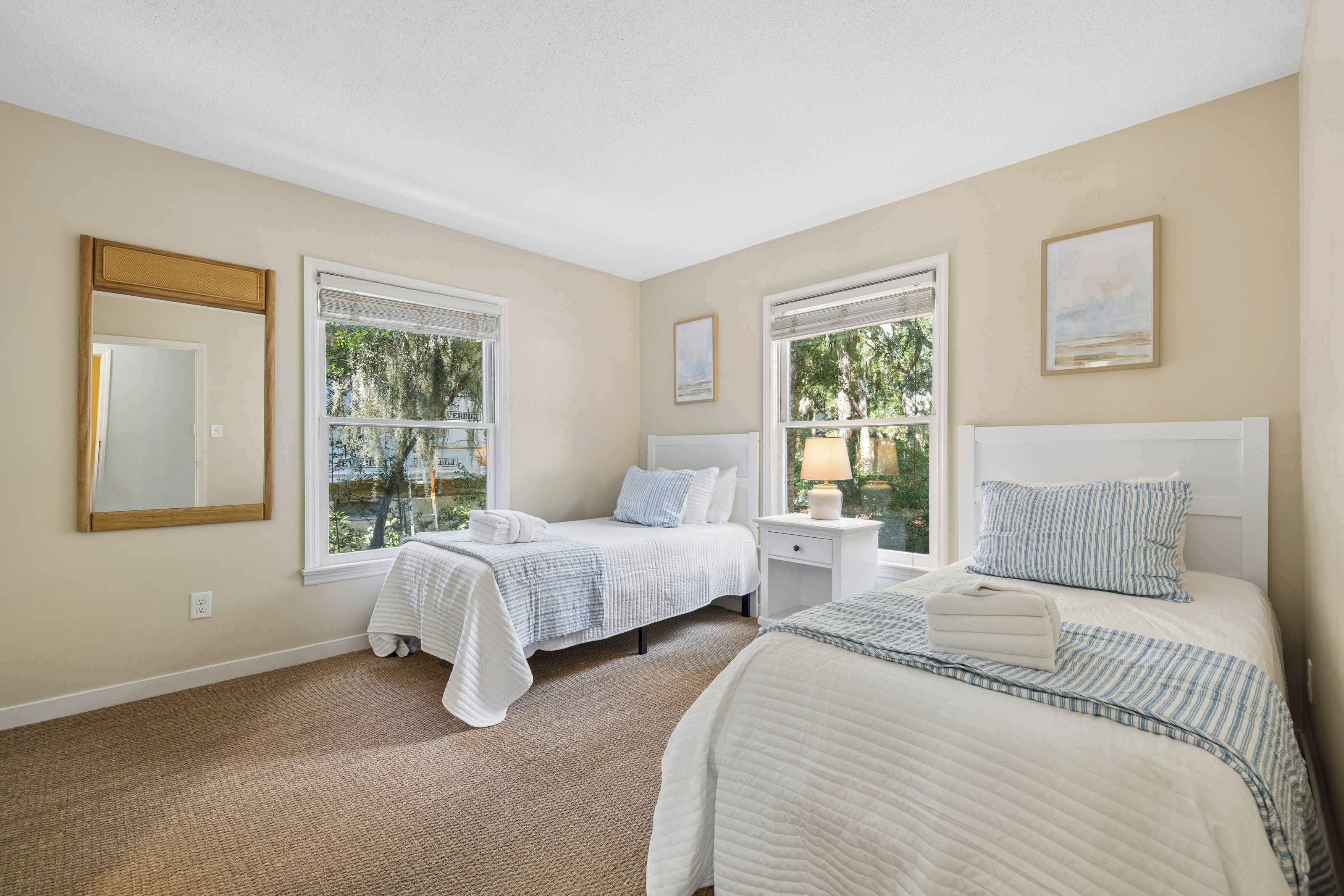 A bedroom with two beds, a nightstand, a mirror, and a window with a view of trees.