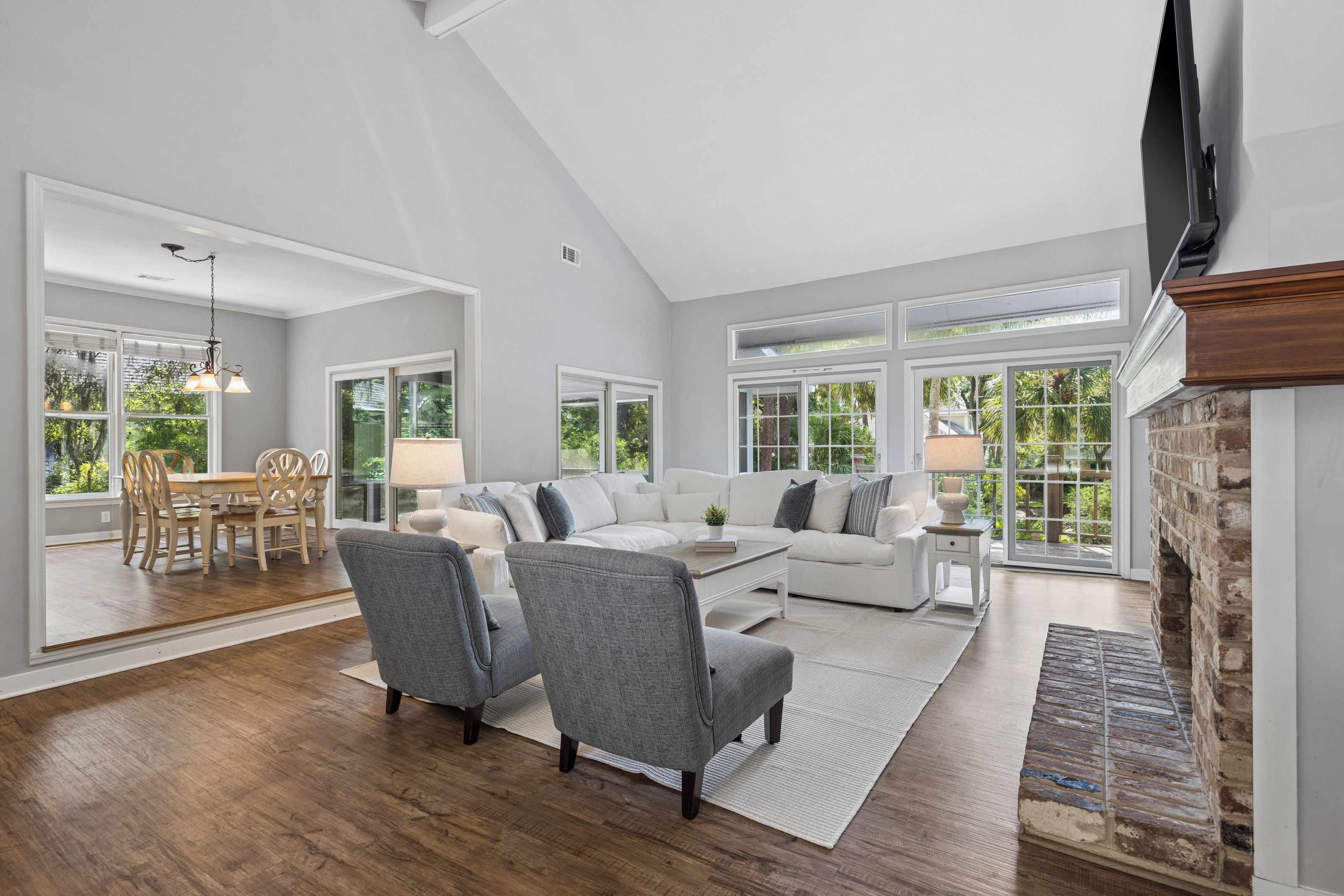 A spacious living room with a high ceiling, large windows, a fireplace, and a dining area with a table and chairs.