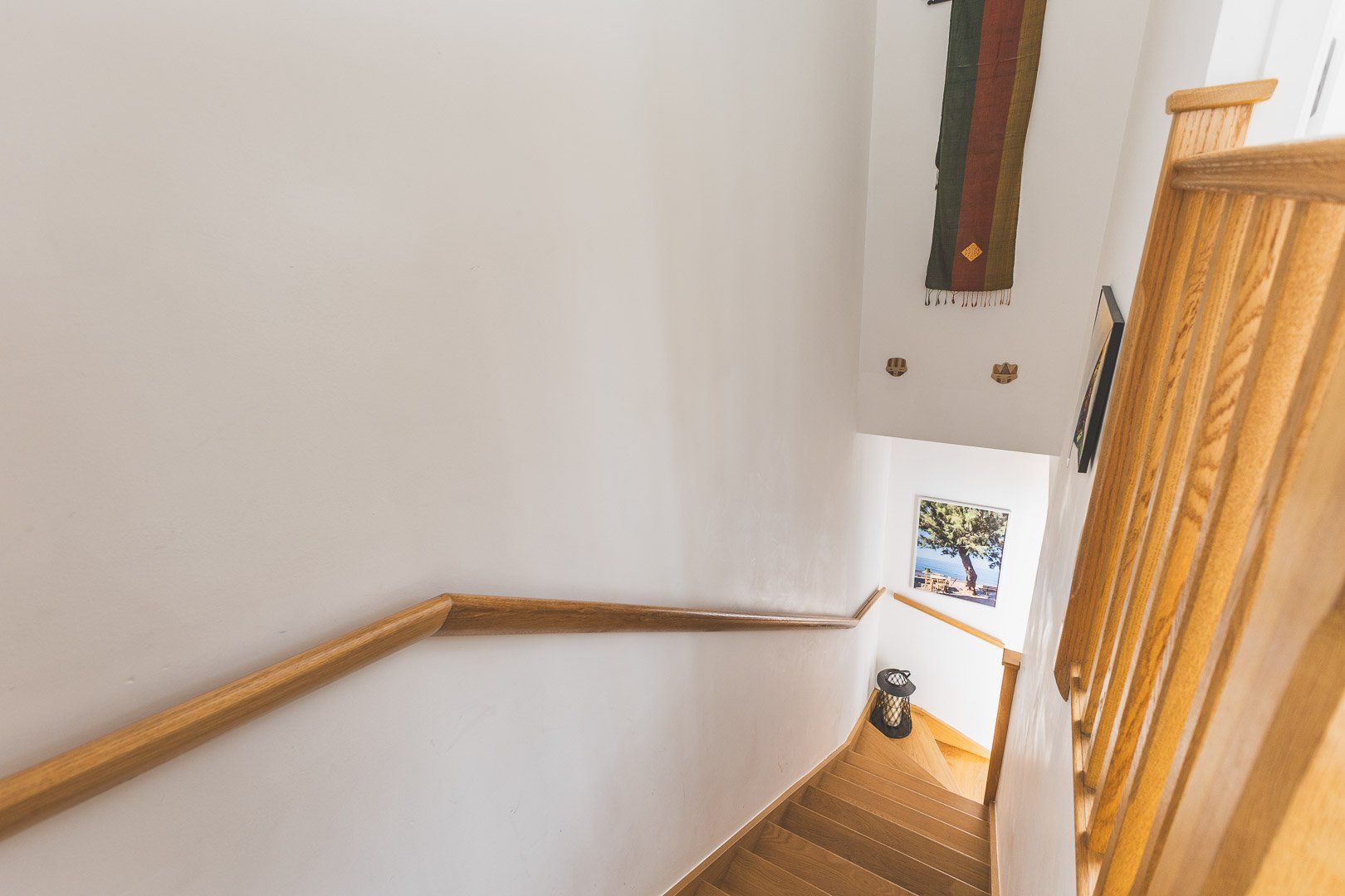 A wooden staircase with a handrail, white walls, and a small picture on the wall.