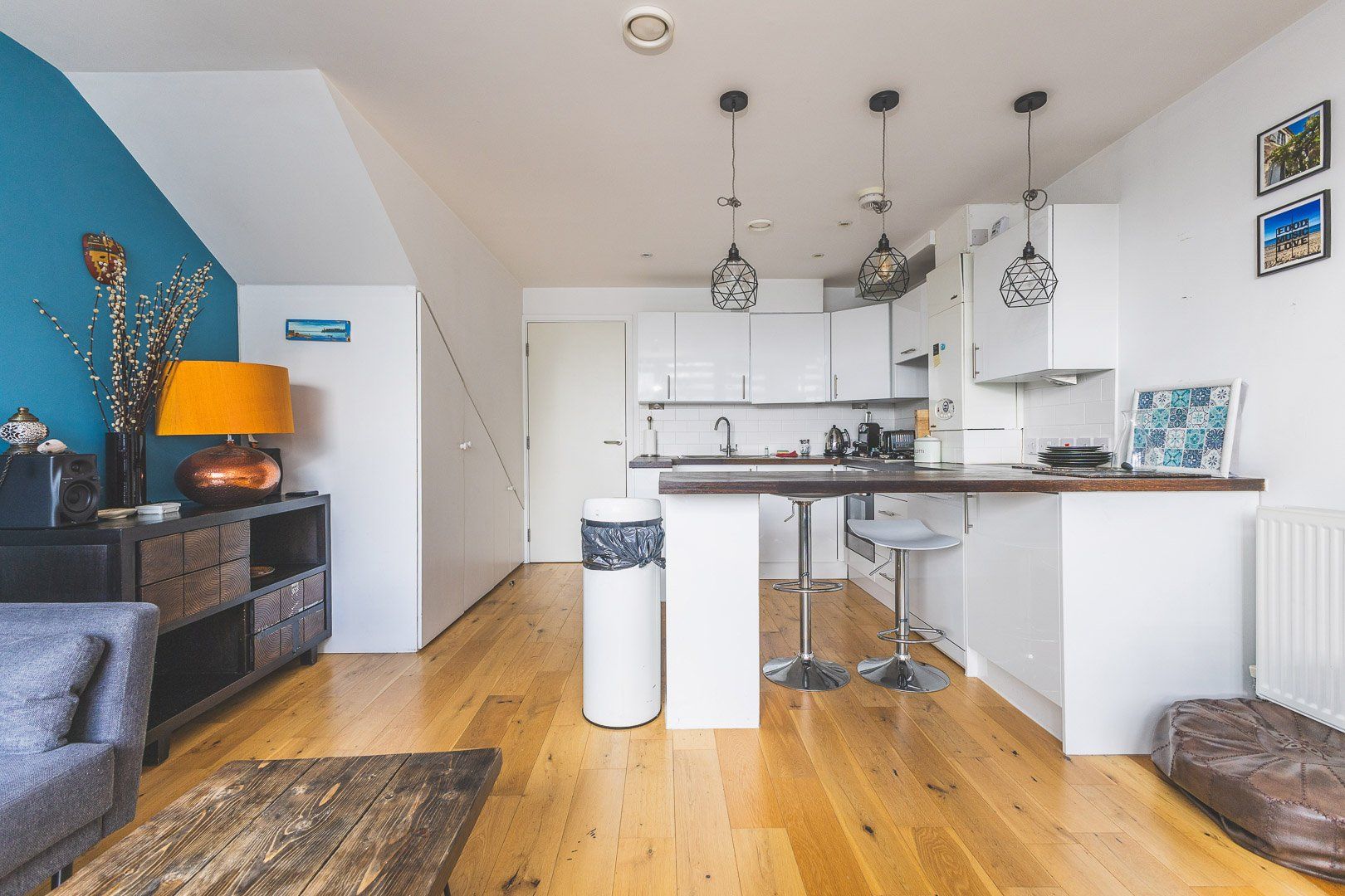Una cocina compacta con una isla central, luces colgantes y vistas al área de estar, que incluye un sofá y una lámpara.