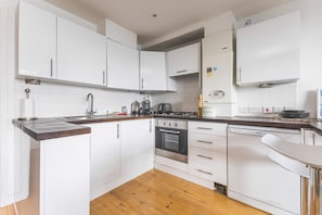 Eine moderne Küche mit weißen Schränken, einer Holz Arbeitsplatte, einem Gasherd, einem Backofen und einem Geschirrspüler.