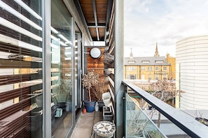 Ein Balkon mit Blick auf ein Gebäude mit einem Turm, Blumentöpfen und einem kleinen Tisch.