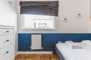 Un dormitorio con cama, radiador, ventana con vistas, cómoda y estante.