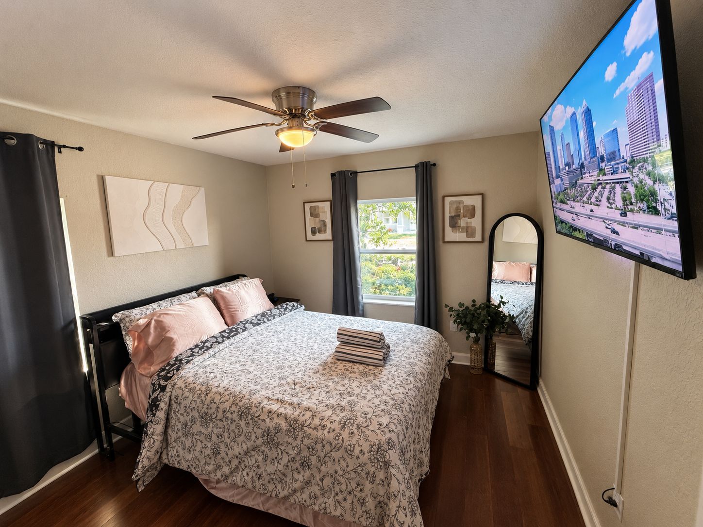 A bedroom with a bed, a ceiling fan, a TV, and a window.
