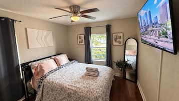 Une chambre à coucher avec un lit, un ventilateur de plafond, une télévision et une fenêtre.