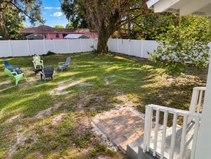 A backyard with a white fence, a tree, and outdoor furniture including chairs and a table.