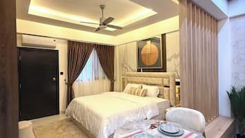 A modern bedroom with a bed, bedside tables, a round dining table with chairs, a ceiling fan, and a large window with curtains.