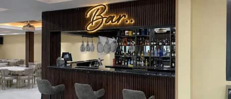 A bar area with a wooden facade, bar stools, and a well-stocked shelf of beverages.