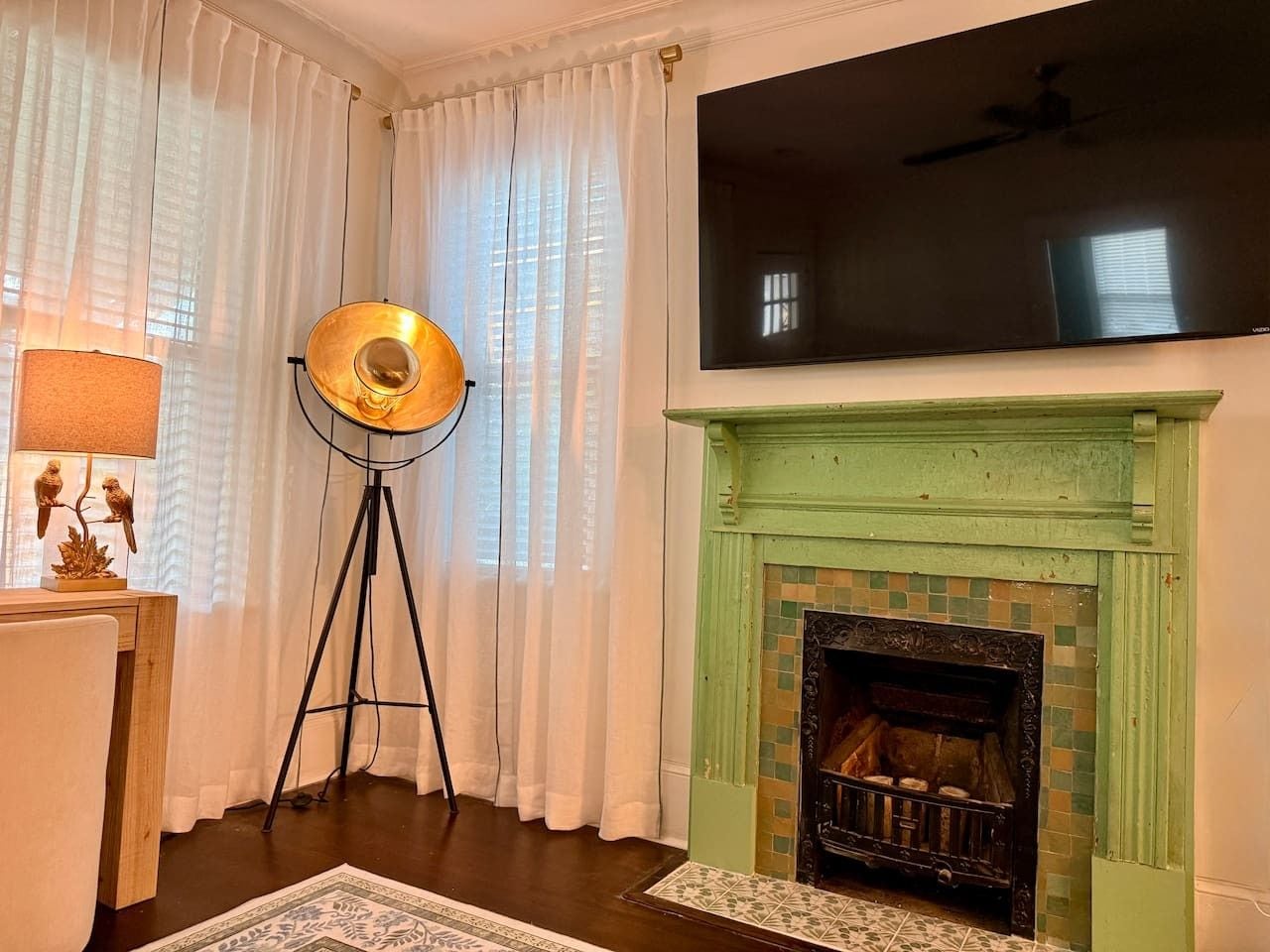 A room with a fireplace, a standing lamp, and a flat-screen TV mounted above it.
