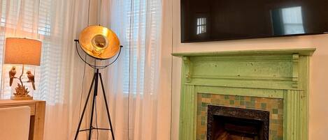 A room with a fireplace, a standing lamp, and a flat-screen TV mounted above it.