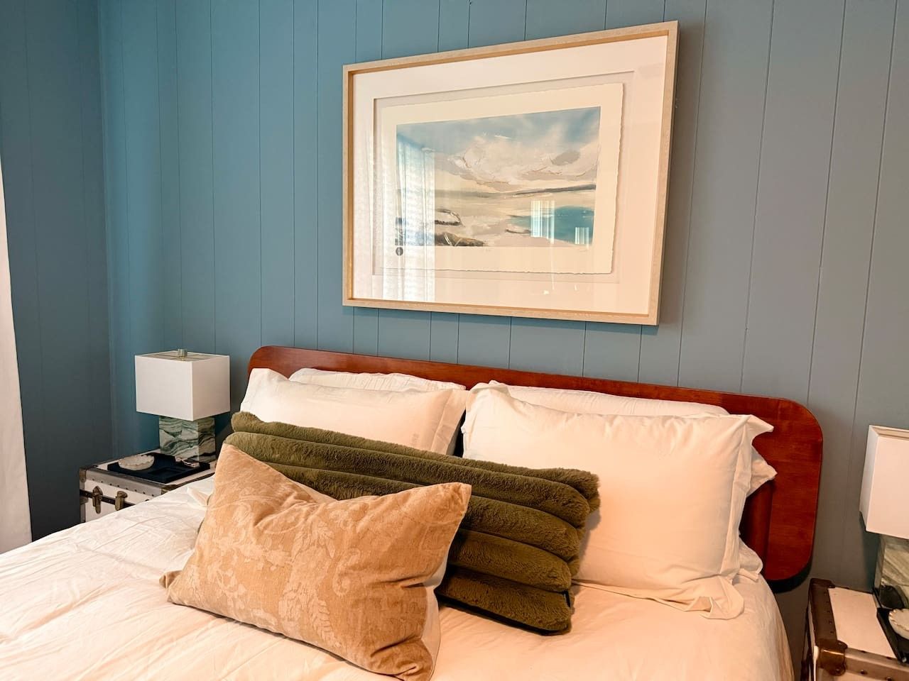 A bed with a wooden headboard, multiple pillows, and a framed picture above it.
