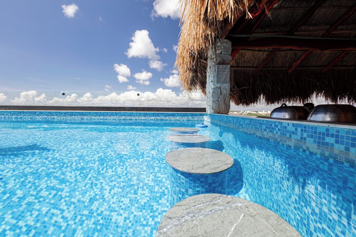 Piscina azul límpida com degraus de pedra levando a uma construção com telhado de palha.