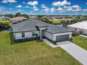 A residential house with a garage, a lawn, and a pond in the background. - New - Lux - Waterfront - Hot Tub - Bikes (Cape Coral)