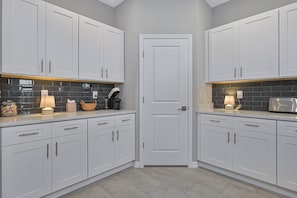 A kitchen with white cabinets, a tiled backsplash, and a door. - New - Lux - Waterfront - Hot Tub - Bikes (Cape Coral)