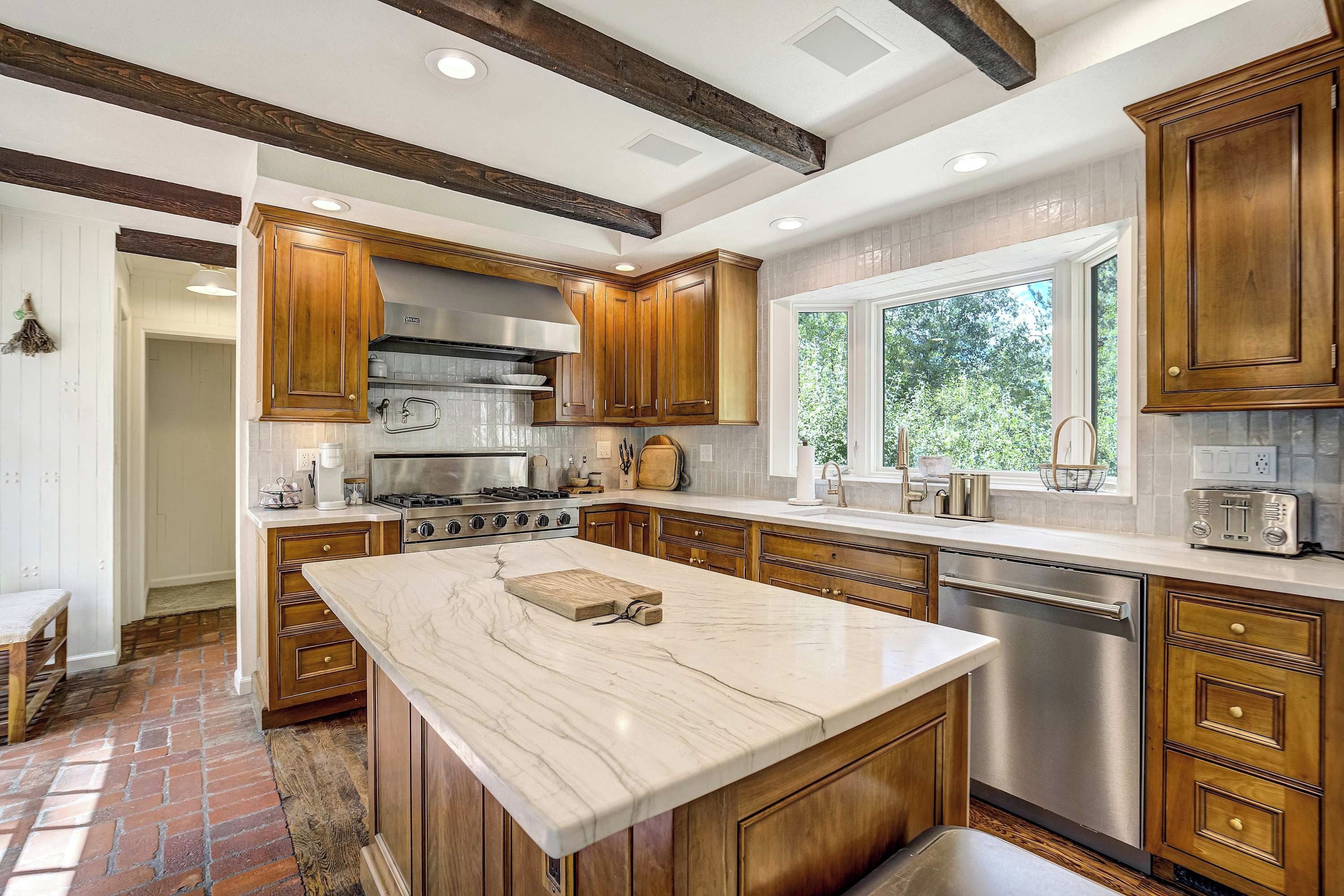 A modern kitchen with a large island, wooden cabinets, stainless steel appliances, and a window providing natural light.