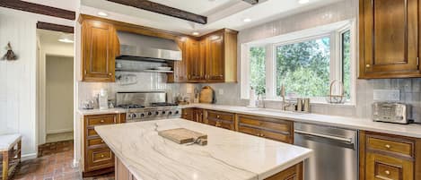 Cozinha moderna com uma ilha grande, armários de madeira, eletrodomésticos de aço inoxidável e janela que oferece iluminação natural.