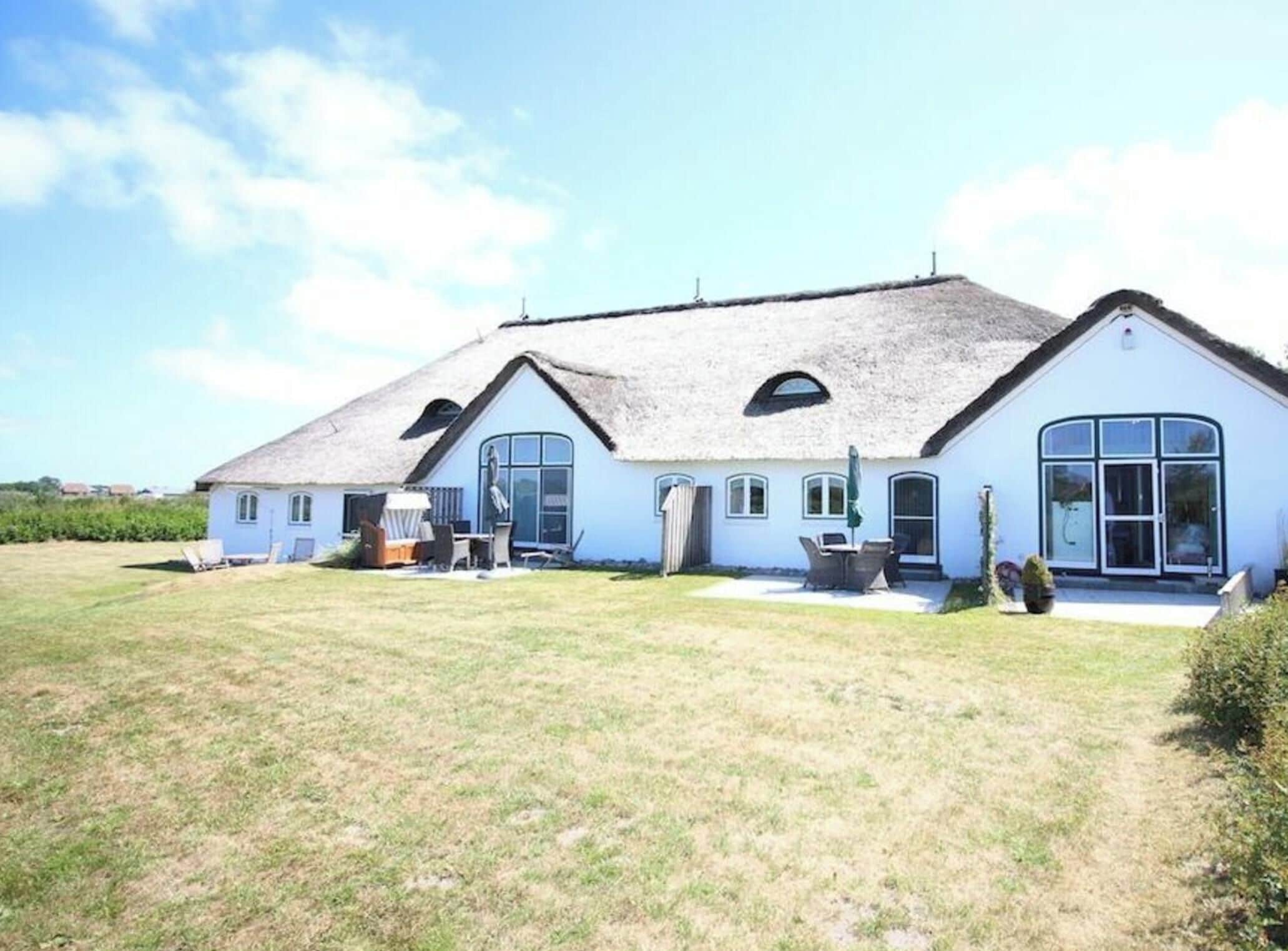 A two-story house with a thatched roof, large windows, and a grassy yard.