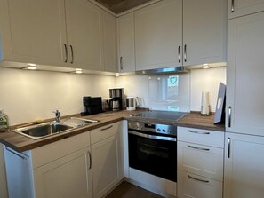 A modern kitchen with white cabinets, stainless steel appliances, and a wooden countertop. - 4 in the Friesenhof - Starfish (St. Peter-Ording)