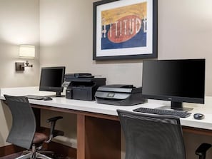 A hotel office with two computer monitors, a printer, a keyboard, and a chair.