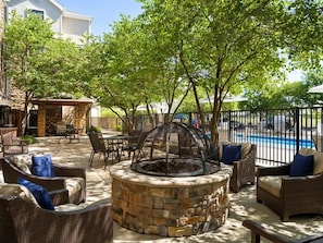 An outdoor patio with stone fire pit seating, a pool, and a covered area.