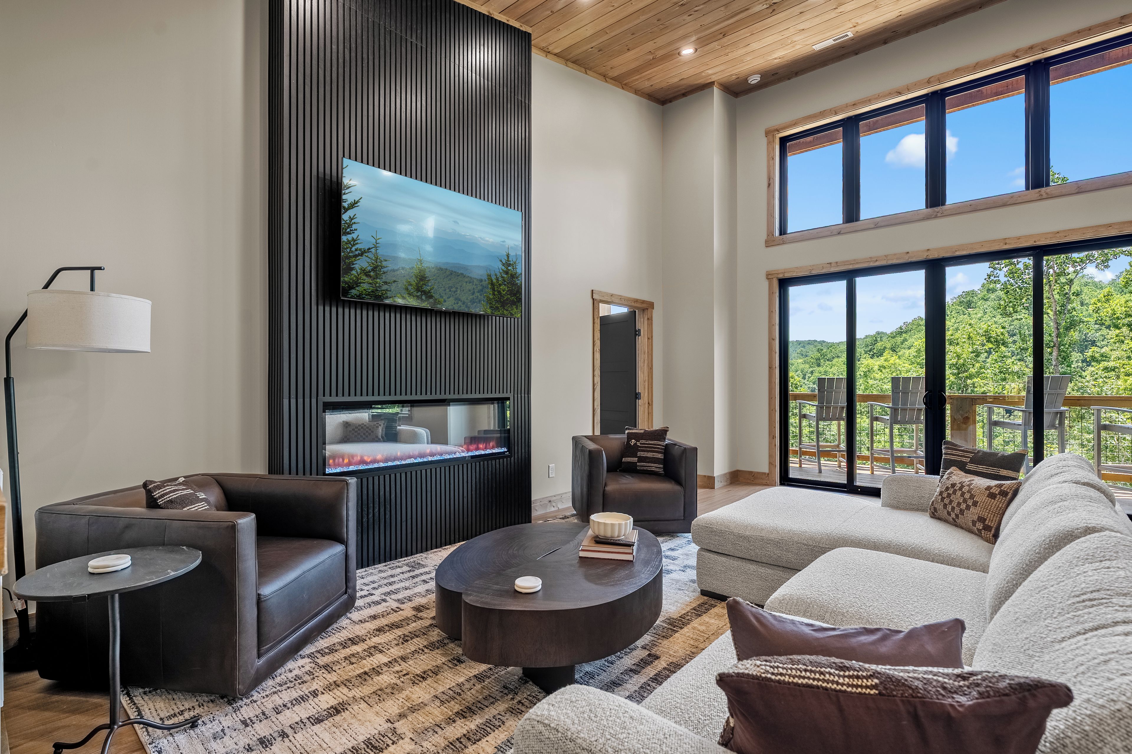 A modern living room with a fireplace, comfortable seating, and large windows offering a view of the outdoors.