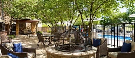 An outdoor patio with stone fire pit seating, a pool, and a covered area.
